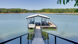 A wooden dock leading to a covered seating area with a view of a calm lake and forested shoreline.