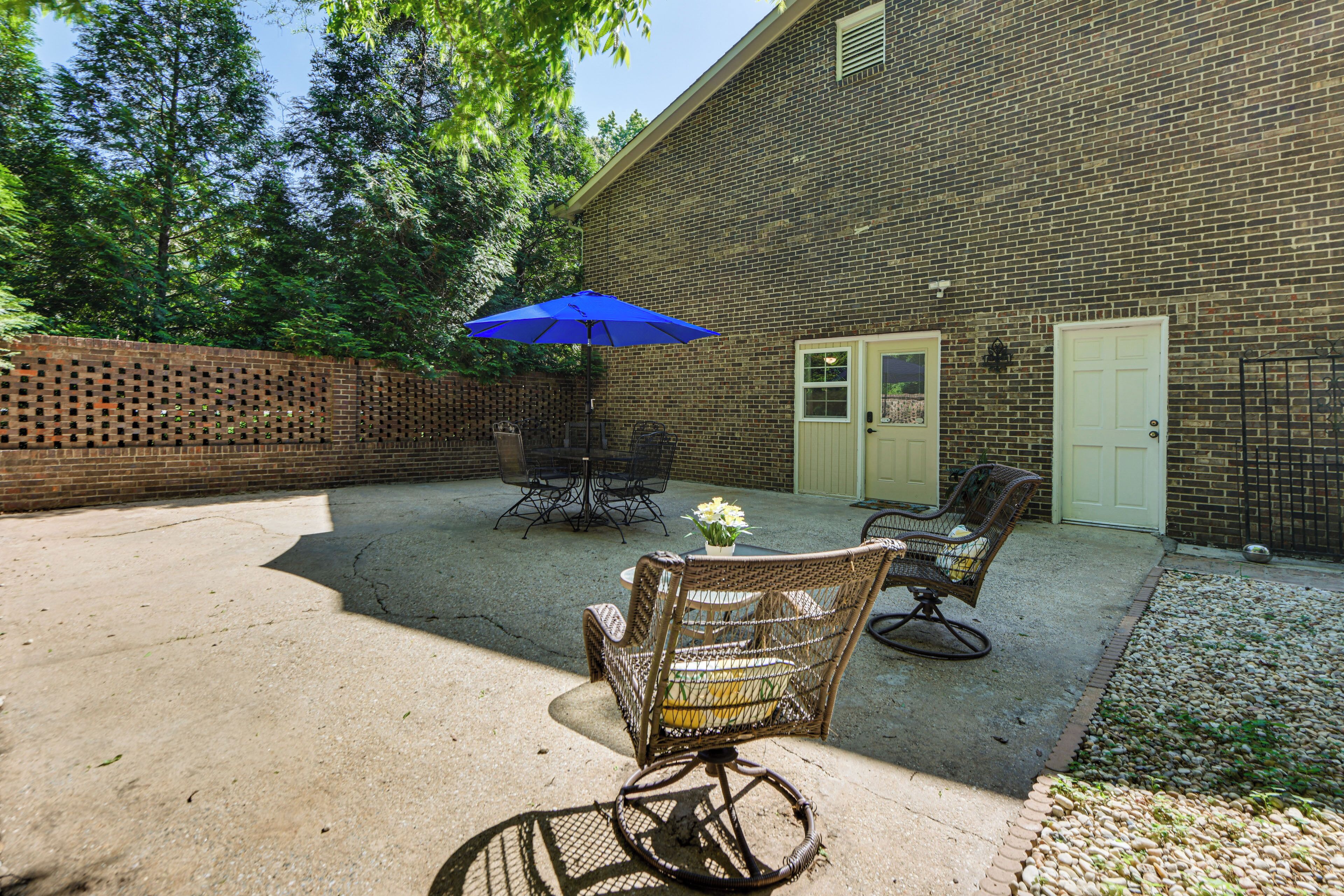 A patio area with a brick wall, outdoor furniture, and a blue umbrella.