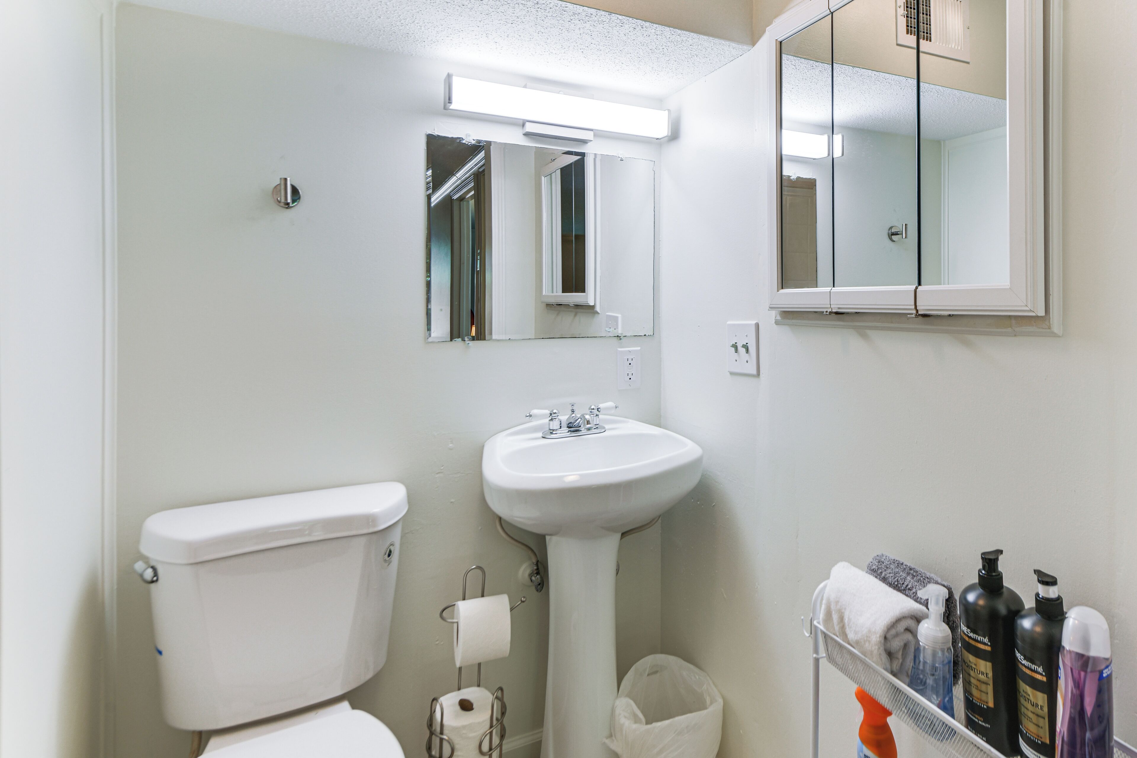 A bathroom with a toilet, sink, mirror, and a shelf with toiletries.