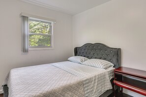 Une chambre à coucher avec un lit, une table de chevet, une fenêtre avec des rideaux et une vue sur la verdure à l’extérieur.