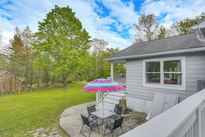 A patio with a table and chairs, an umbrella, and a house with a window. - Deck & Patio! Wurtsboro Haven Near Lakes & Trails (Wurtsboro)
