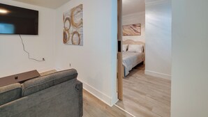 Una habitación moderna con televisión de pantalla plana, arte abstracto, un sofá y una cama con cabecera.
