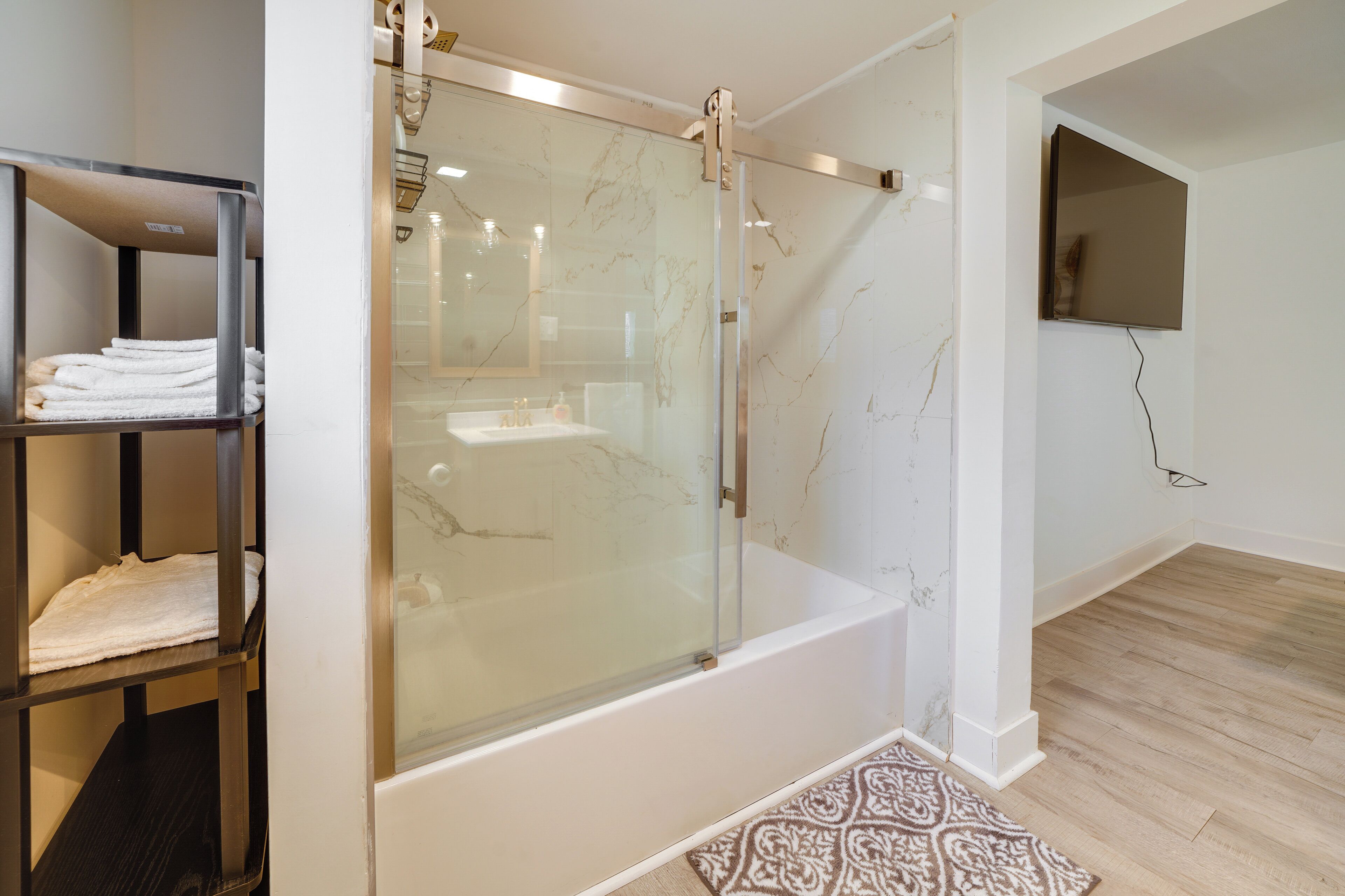 A modern bathroom with a glass-enclosed shower, a white bathtub, and a wooden floor.
