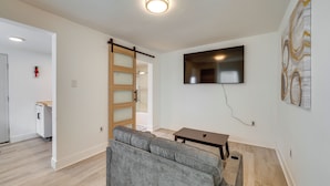 Un moderno salón con un sofá gris, un televisor de pantalla plana montado en la pared y una puerta corredera con marco de madera.