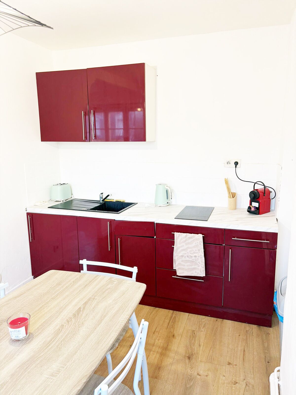 A compact kitchen with a wooden table, white chairs, a red cabinet, and a kettle.