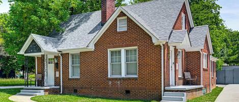A two-story brick house with a front porch, a chimney, and a small front yard.