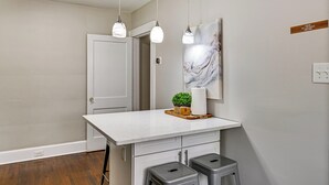 A kitchen with a white countertop, two stools, pendant lights, a door, and a wall-mounted sign. - Charlotte Duplex Close to Uptown and Sports (Charlotte)