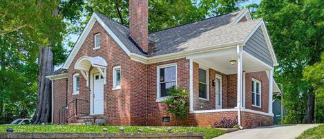 A brick house with a chimney, a porch, and a well-maintained lawn.