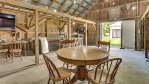 L’intérieur d’une grange rustique, avec une table à manger en bois, des chaises et une grande fenêtre.