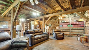 Un intérieur rustique avec des poutres en bois, des canapés en cuir, une bibliothèque et une échelle.