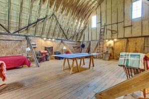 A loft bedroom with a sloped ceiling, wooden beams, a ping pong table, a bed, and a ladder.