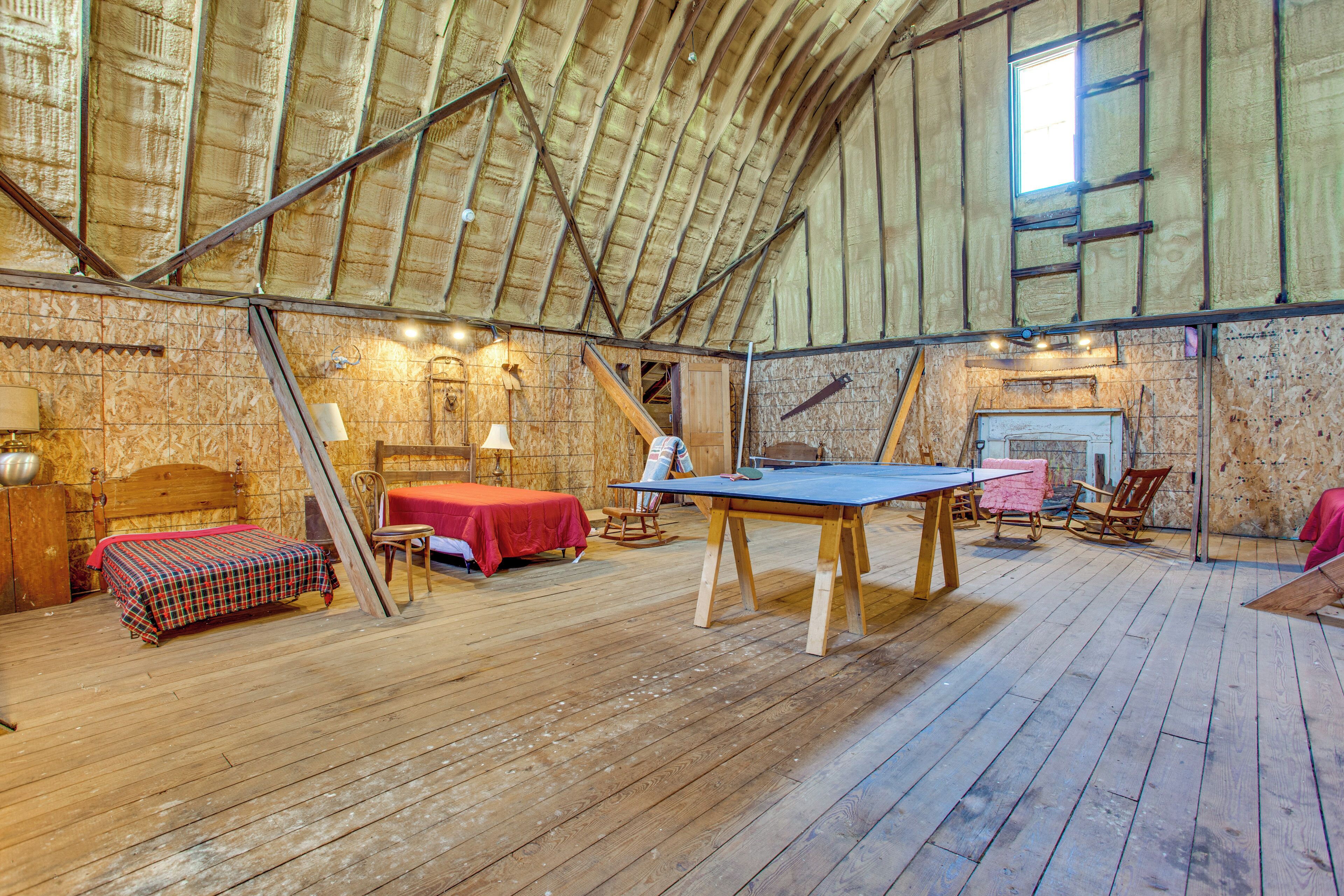A rustic room with a wooden floor, a ping pong table, a bed with a plaid bedspread, and a fireplace.