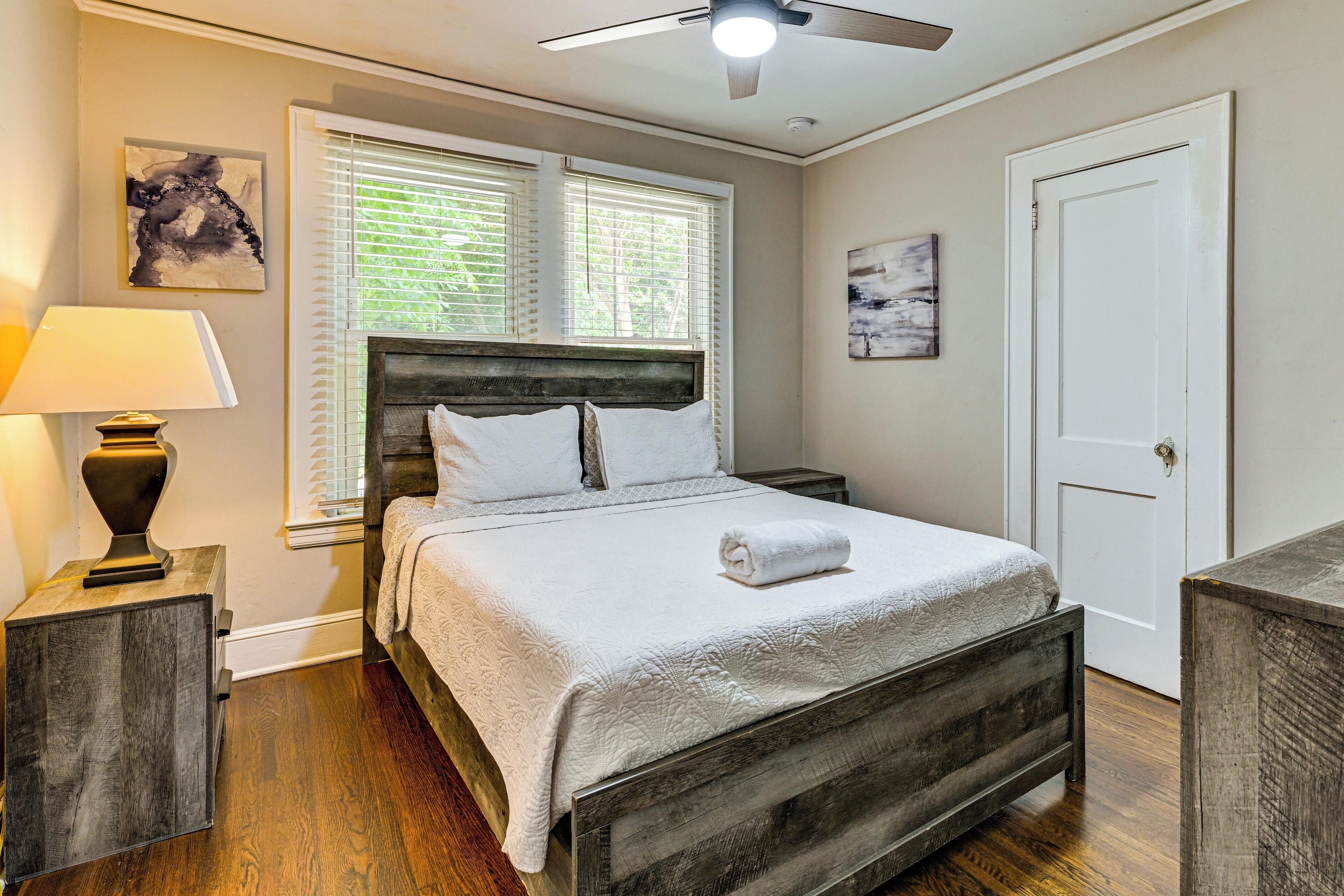 A bedroom with a bed, a nightstand, a lamp, a ceiling fan, and a door.