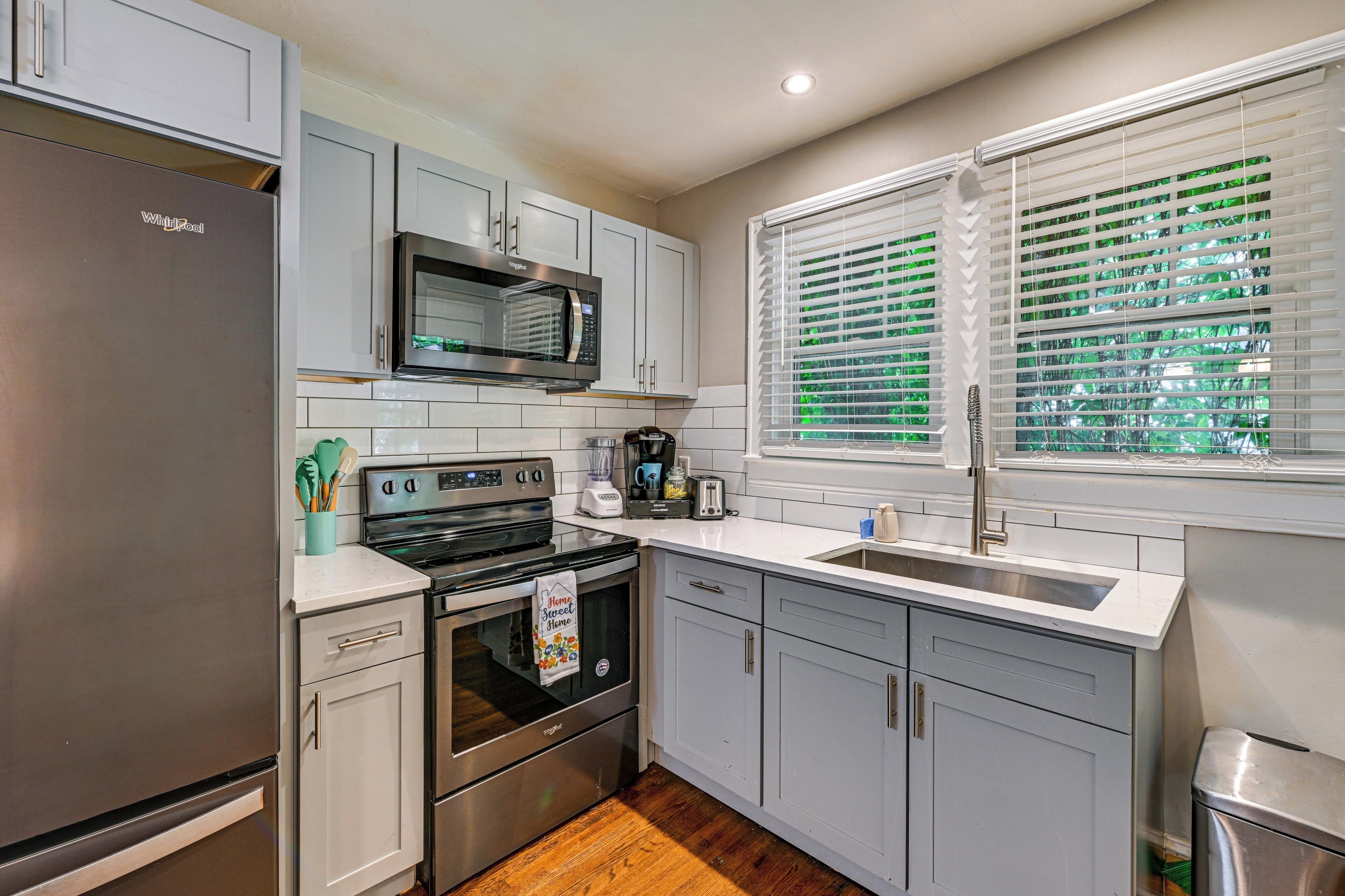 A modern kitchen with stainless steel appliances, white cabinetry, and a window with blinds.