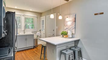 A kitchen with a white island, bar stools, pendant lights, and a large window with blinds.