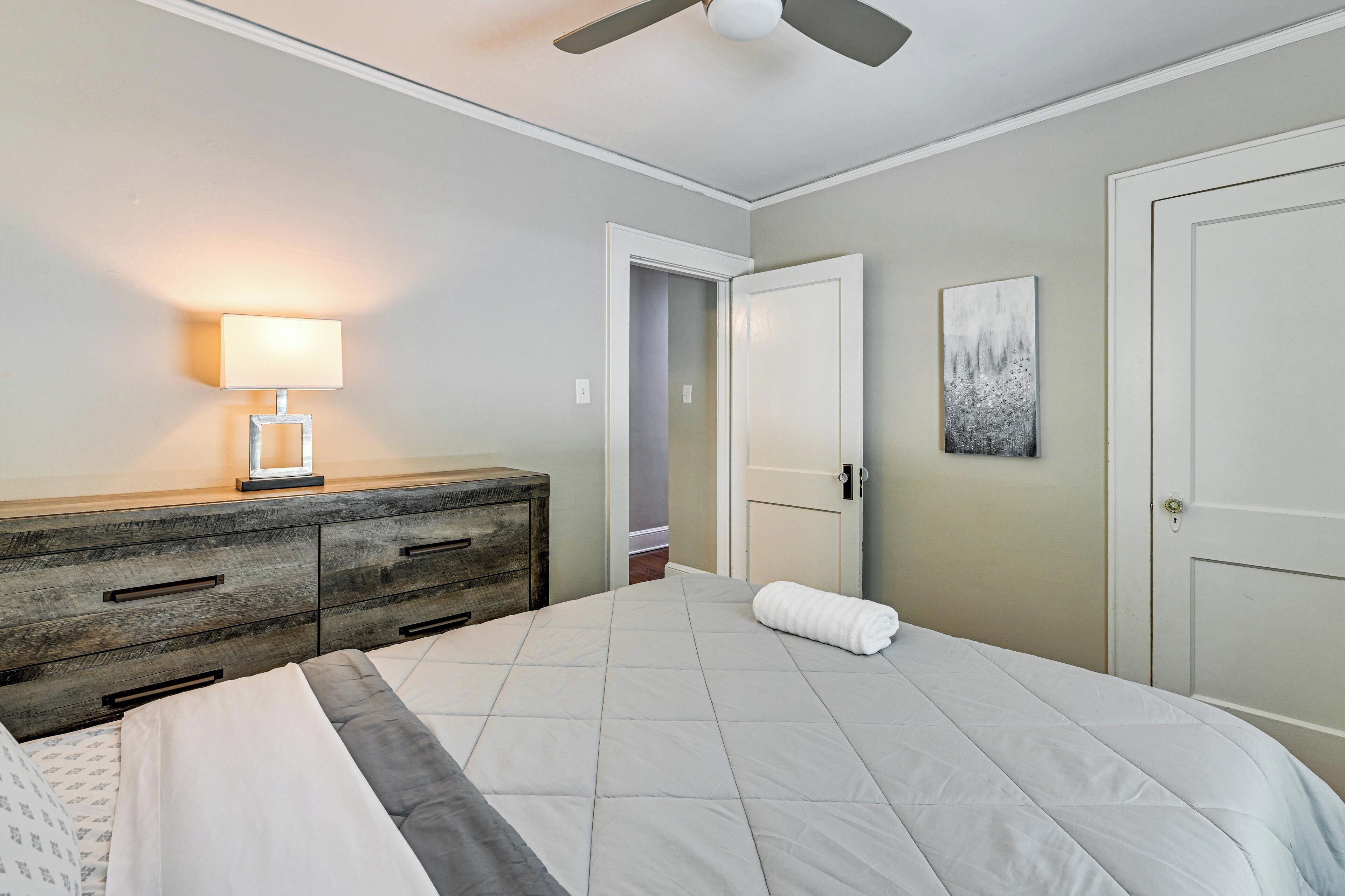 A bedroom with a bed, a dresser, a nightstand, a ceiling fan, and a door.