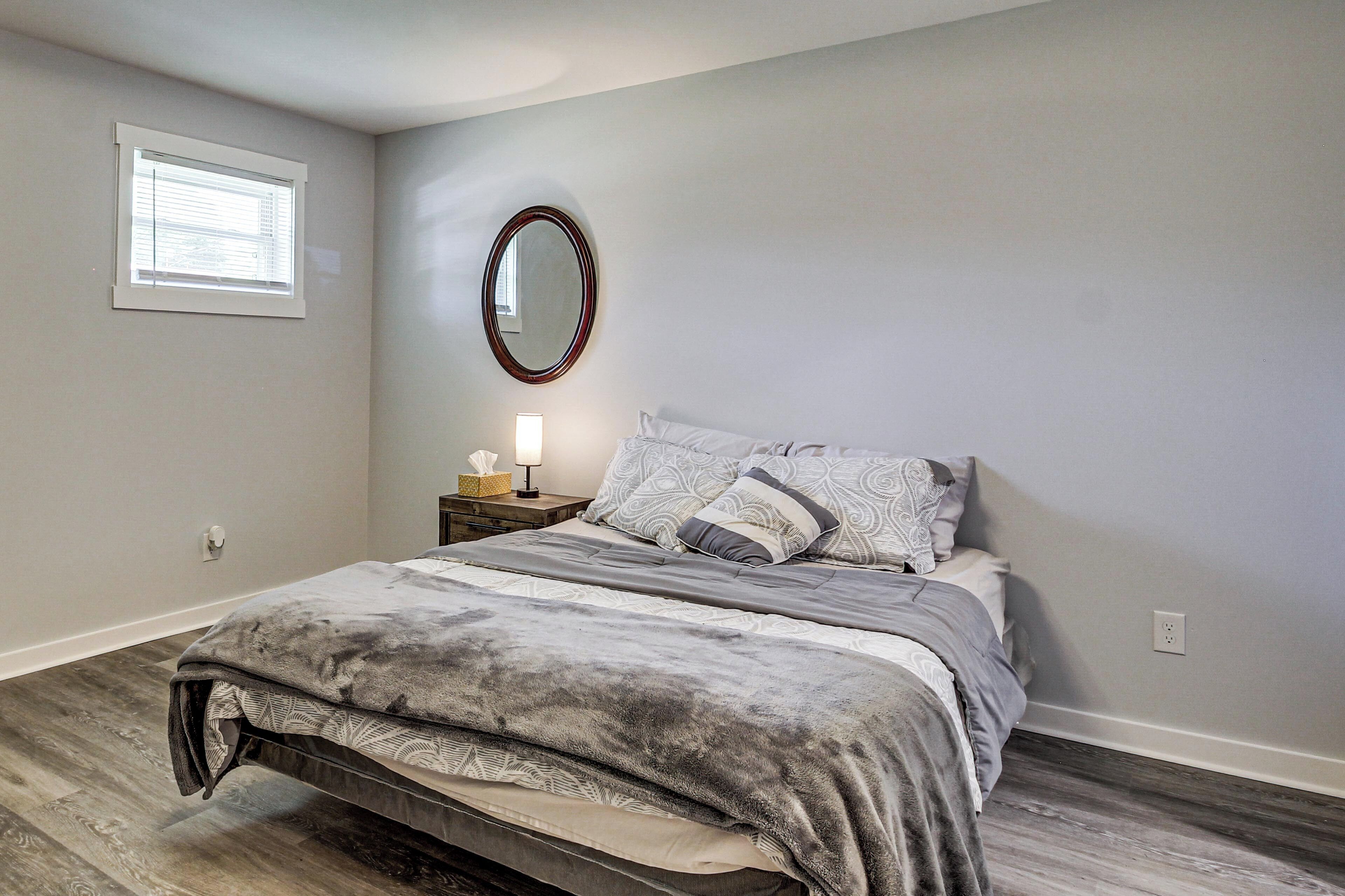 Une chambre à coucher comprenant un lit, une table de chevet, un miroir, une fenêtre et une prise électrique.