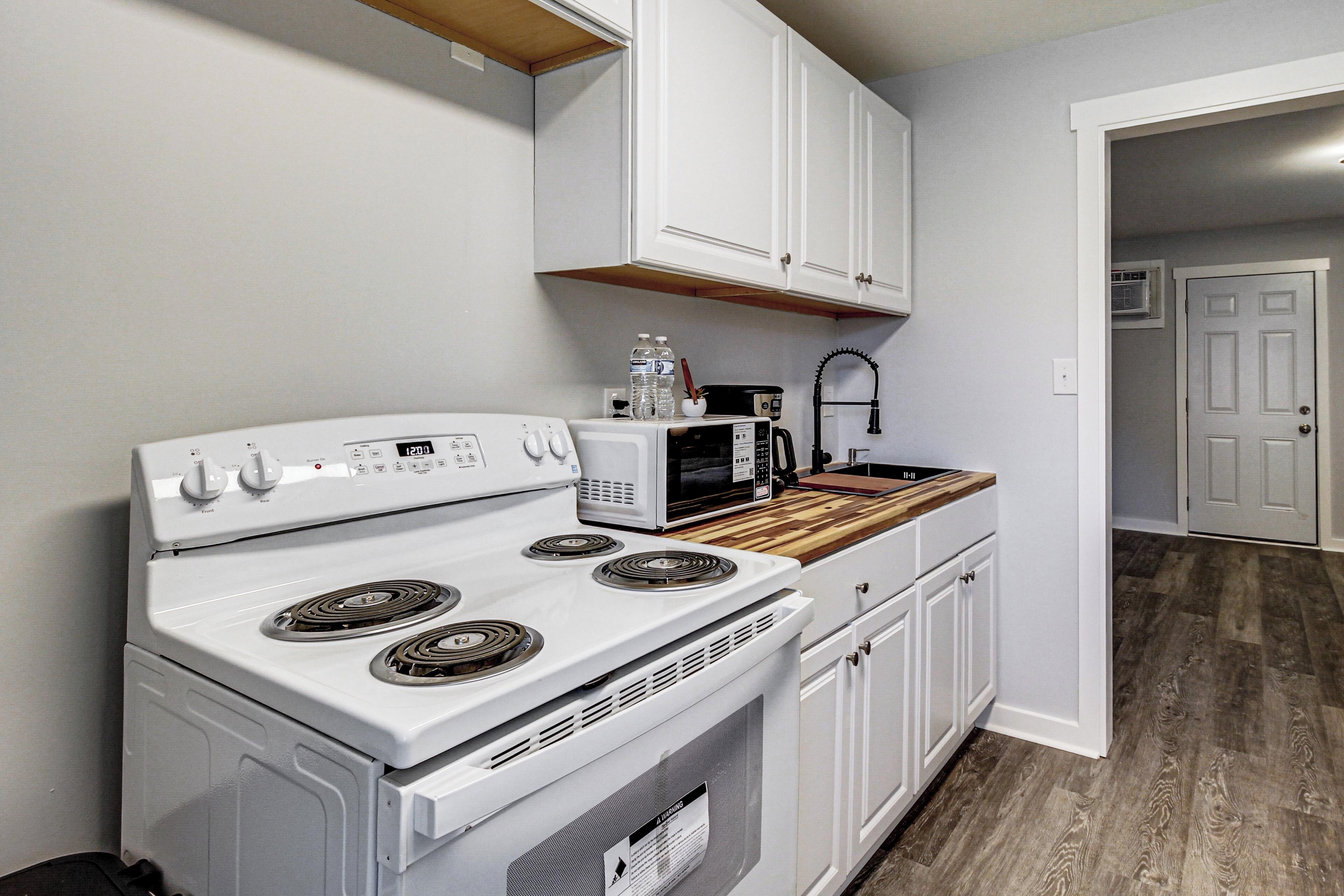 A kitchen with white cabinets, a microwave, a stove, and a wooden countertop.