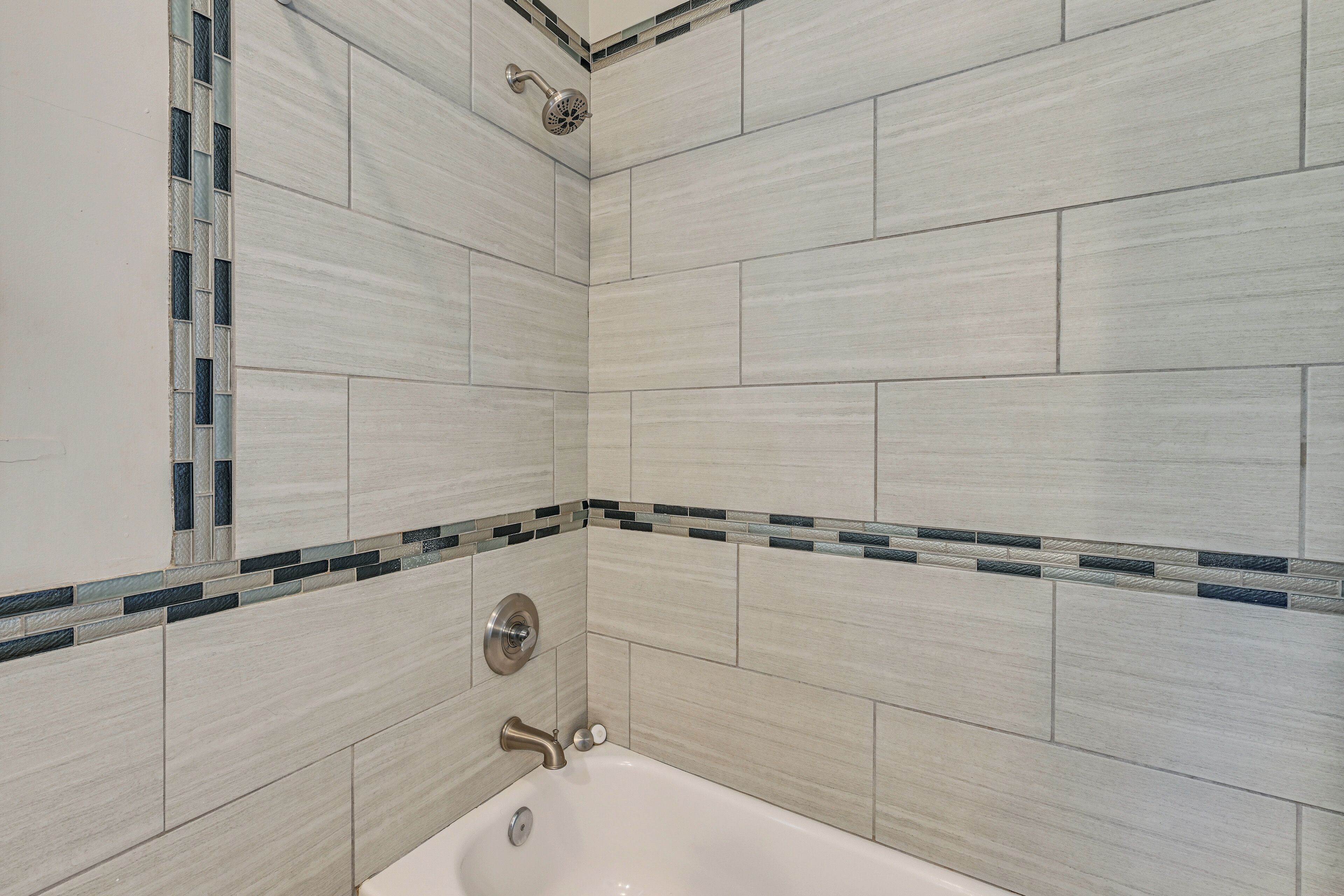 A bathroom with a bathtub, a showerhead, and a tiled wall with a decorative border.