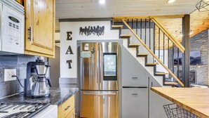 Une cuisine moderne équipée d’un réfrigérateur en acier inoxydable, d’une machine à café et d’un escalier en bois.