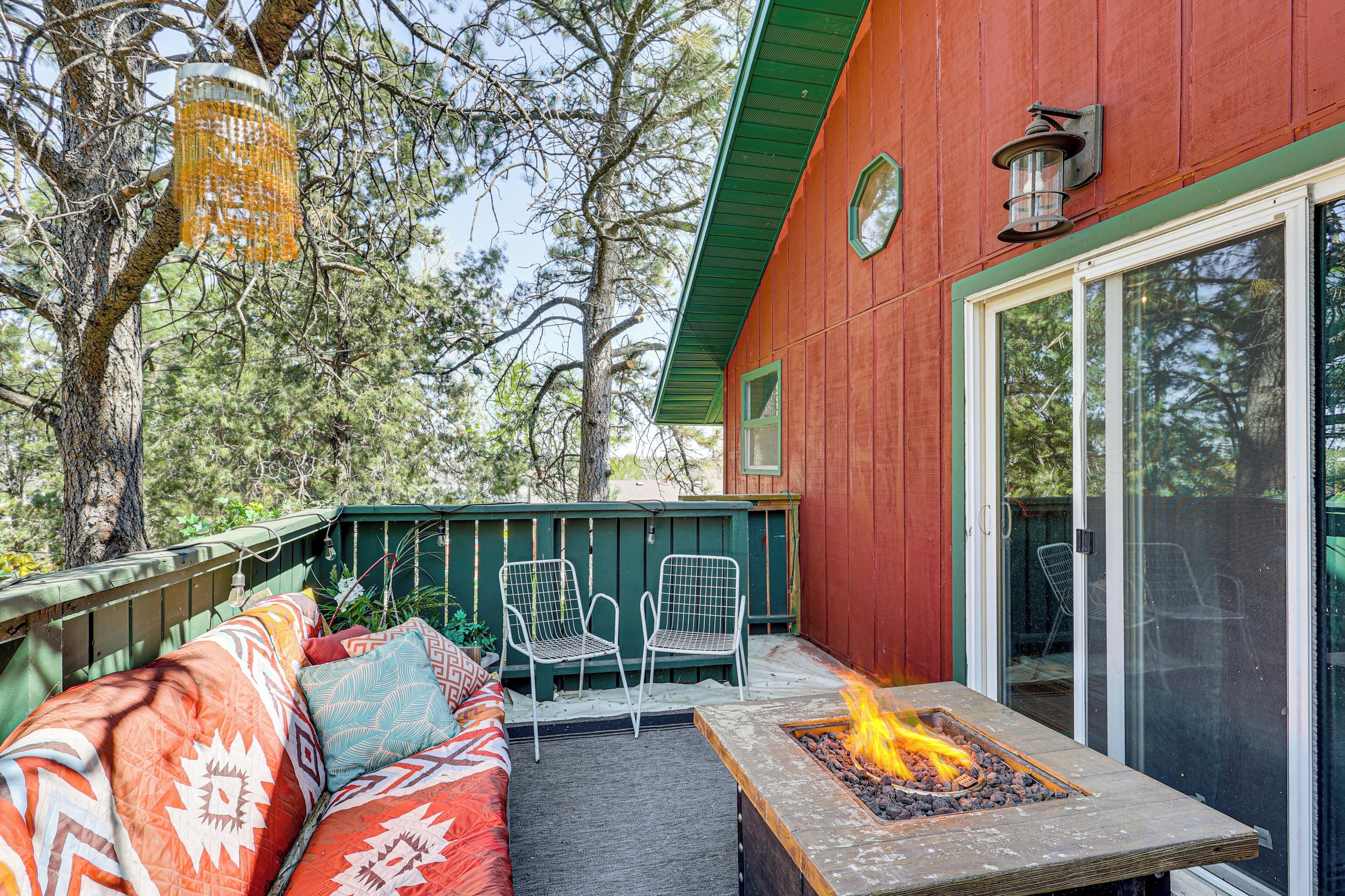 A covered outdoor seating area with a fire pit, a wooden deck, and a red building with a sliding glass door.