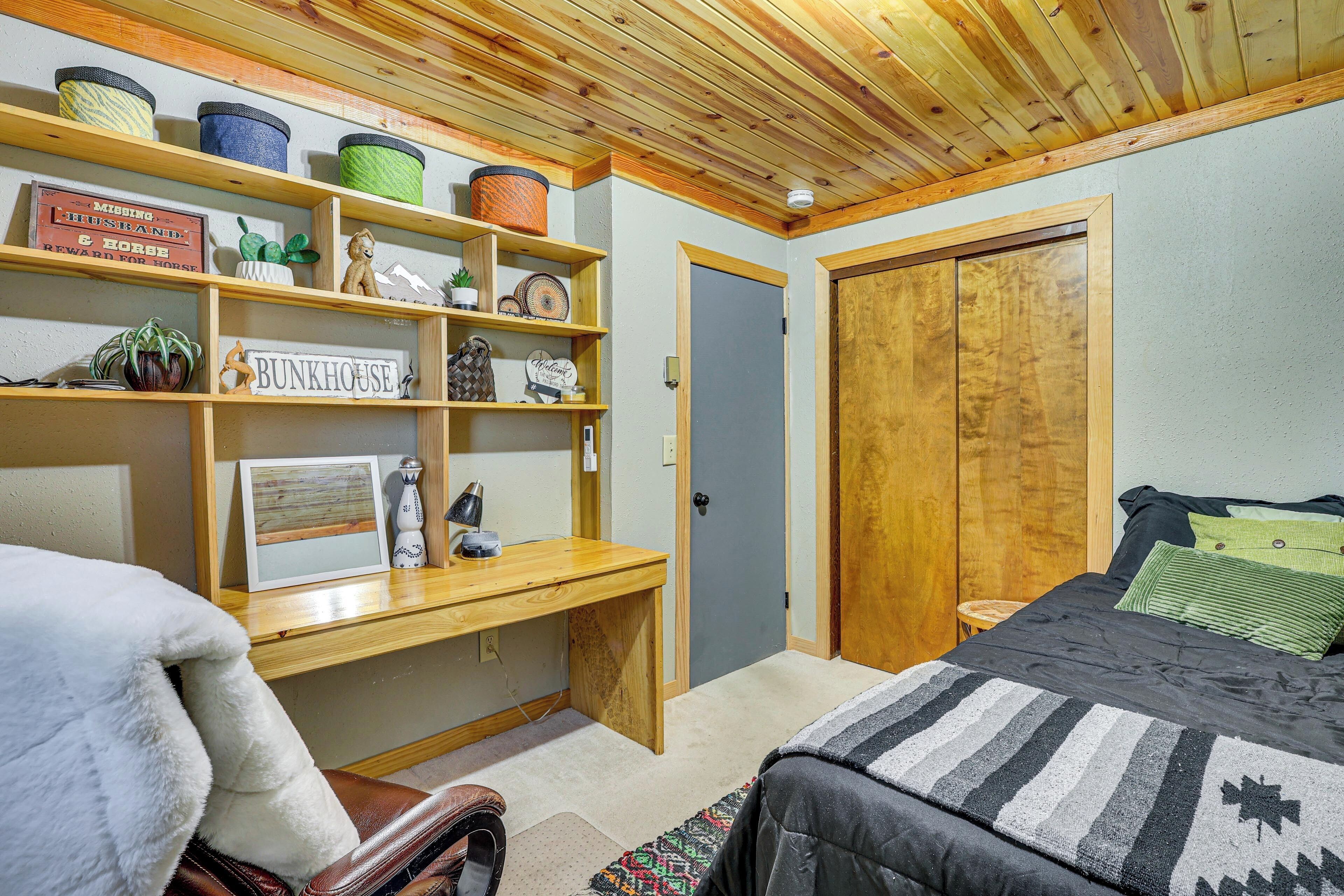 A bedroom with a bed, a desk, a chair, a wardrobe, and shelves with various items.