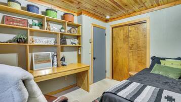 A bedroom with a bed, a desk, a chair, a wardrobe, and shelves with various items.