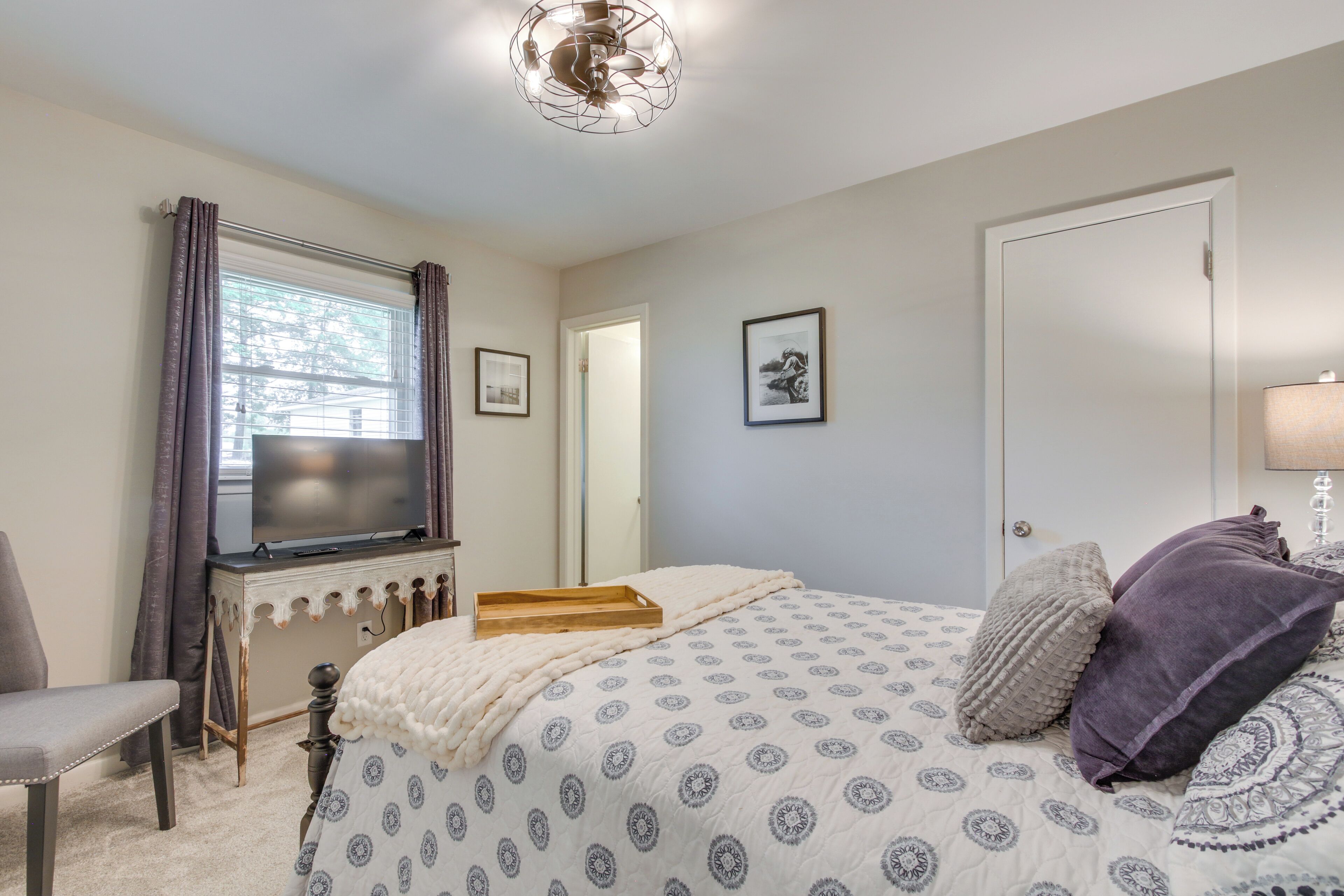 Quarto com cama, escrivaninha, cadeira, televisão e porta.