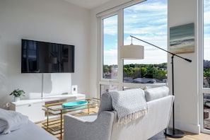 Ein modernes Wohnzimmer mit Flachbildfernseher, einer Couch, einem Couchtisch und einem großen Fenster mit Blick auf die Stadt.