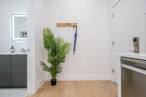 Eine moderne Küche mit grauen Schränken, Holzboden, einem Topf mit Pflanze, einem Holz-Kleiderhaken mit Regenschirm und einer Tür mit digitalem Schloss.