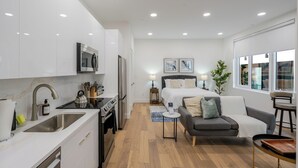 Eine moderne Küche mit Spüle, Herd und Mikrowelle, ein kleiner Essbereich mit Tisch und Stühlen, eine Couch und ein Bett mit Nachttisch.