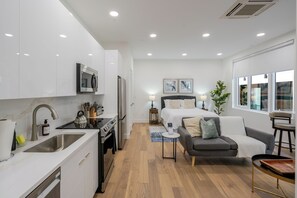 Eine moderne Küche mit Spüle, Herd und Mikrowelle, ein kleiner Essbereich mit Tisch und Stühlen, eine Couch und ein Bett mit Nachttisch.