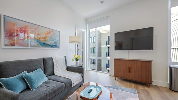 Ett modernt vardagsrum med en grå soffa, ett soffbord i glas, ett träskåp och en stor TV med platt skärm.