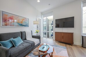 A modern living room with a gray sofa, a glass coffee table, a wooden cabinet, and a large flat-screen TV.