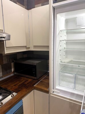 A kitchen with a microwave, a stove, and a refrigerator with shelves. - Jacuzzi & Balcony — Rehab Apt Near Top Malls&Dining (Cairo Governorate)