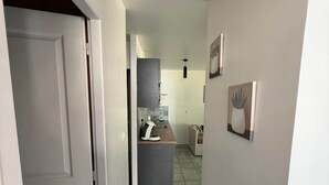 Un pasillo con una puerta a la izquierda, una zona de cocina en el centro y una pared con dos cuadros enmarcados a la derecha.