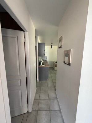 Un couloir avec une porte à gauche, un espace cuisine au centre et un mur orné de deux tableaux encadrés à droite.