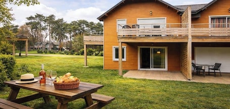 A wooden house with a balcony, a patio with outdoor furniture, and a picnic table with food and drinks.. L'Escapade Gite 6 pers