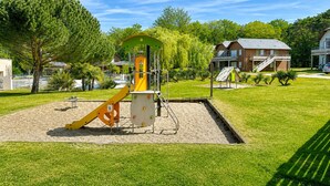 Un parque infantil con estructuras para escalar y toboganes, rodeado de césped y árboles.