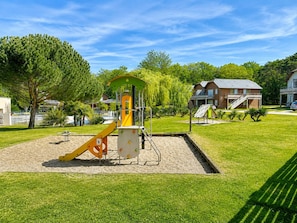 Une aire de jeux avec des structures d’escalade et des toboggans, entourée d’herbe verte et d’arbres.