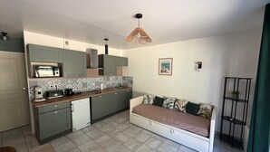 Un espacio habitable compacto con kitchenette, un sofá, una mesa de comedor y una lámpara colgante.
