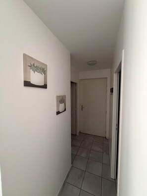 Un couloir aux murs blancs, doté d’un sol carrelé et orné de deux œuvres d’art encadrées.