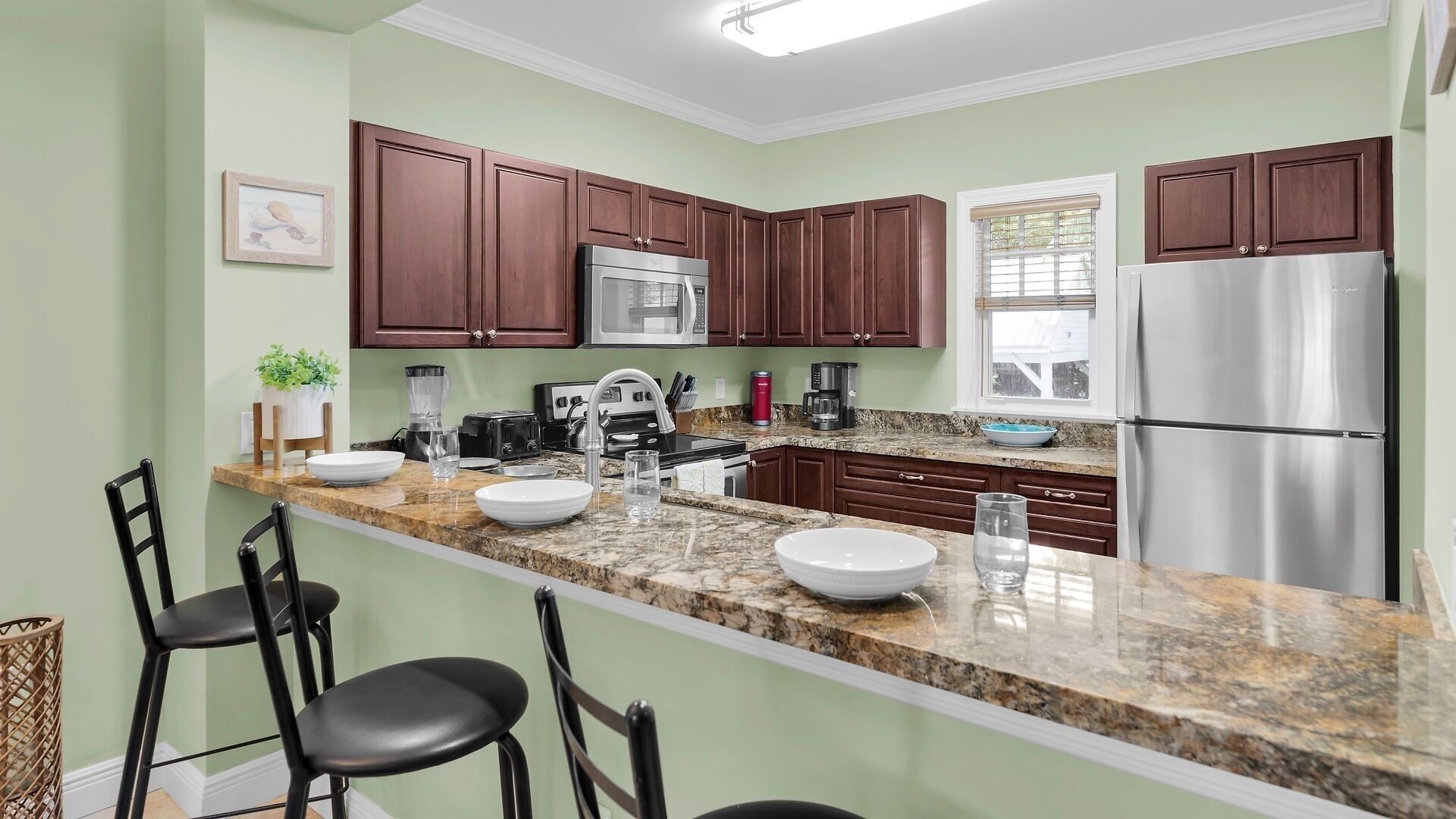 A kitchen with granite countertops, stainless steel appliances, dark wooden cabinets, and a bar stool seating area.