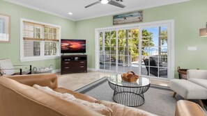 Ein Wohnzimmer mit Fernseher, einer Couch, einem Couchtisch und Blick durch große Schiebetüren auf eine Terrassenanlage.