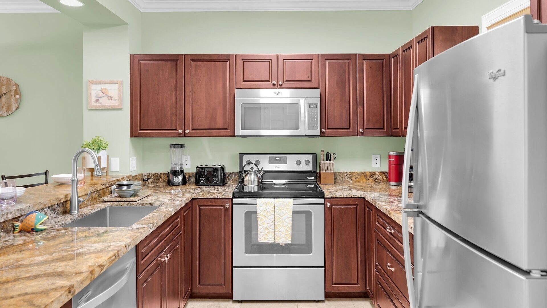 A kitchen with wooden cabinets, a stainless steel refrigerator, a microwave, an oven, and a granite countertop.