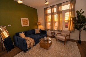A living room with a sofa, armchair, coffee table, and a potted plant.