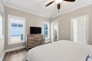 A bedroom with a large bed, a wooden dresser, a television, and a ceiling fan.