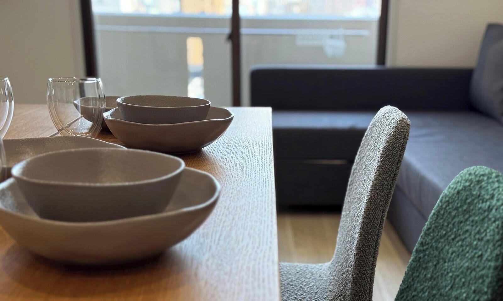 Een eethoek met een tafel gedekt met kommen en glazen, een grijze stoel en een bank op de achtergrond.