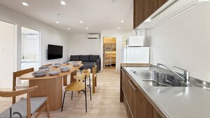 A modern kitchen with a dining area, wooden cabinets, a built-in microwave, and a large stainless steel sink. - Lafort Honkawa (Hiroshima City)