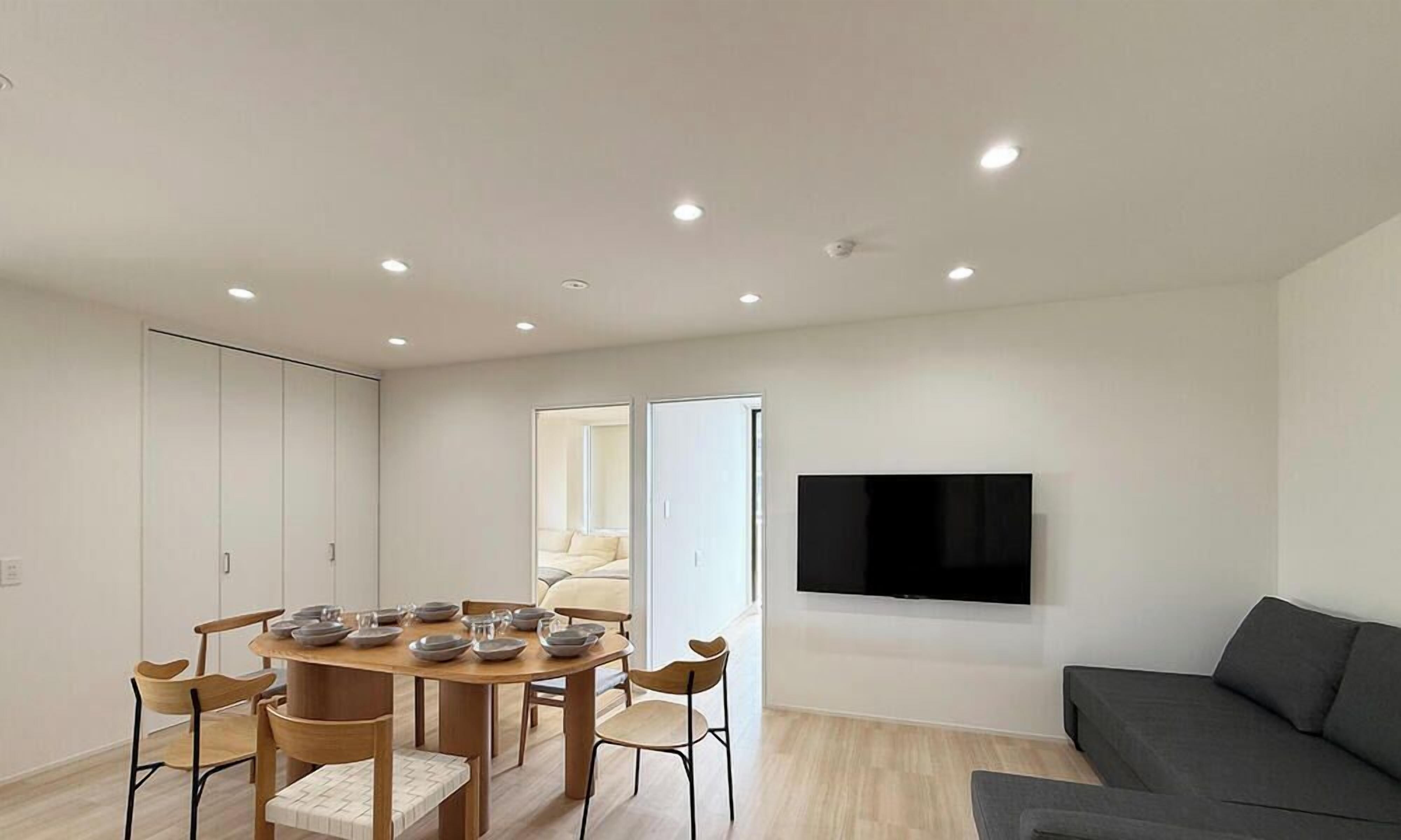 A modern living space with a dining area, a sofa, and a TV mounted on the wall.